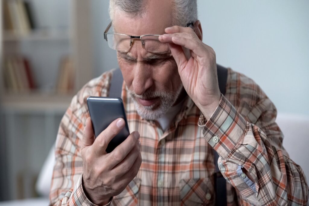 Senior man squinting to read text on smartphone, illustrating common vision challenges like macular degeneration.