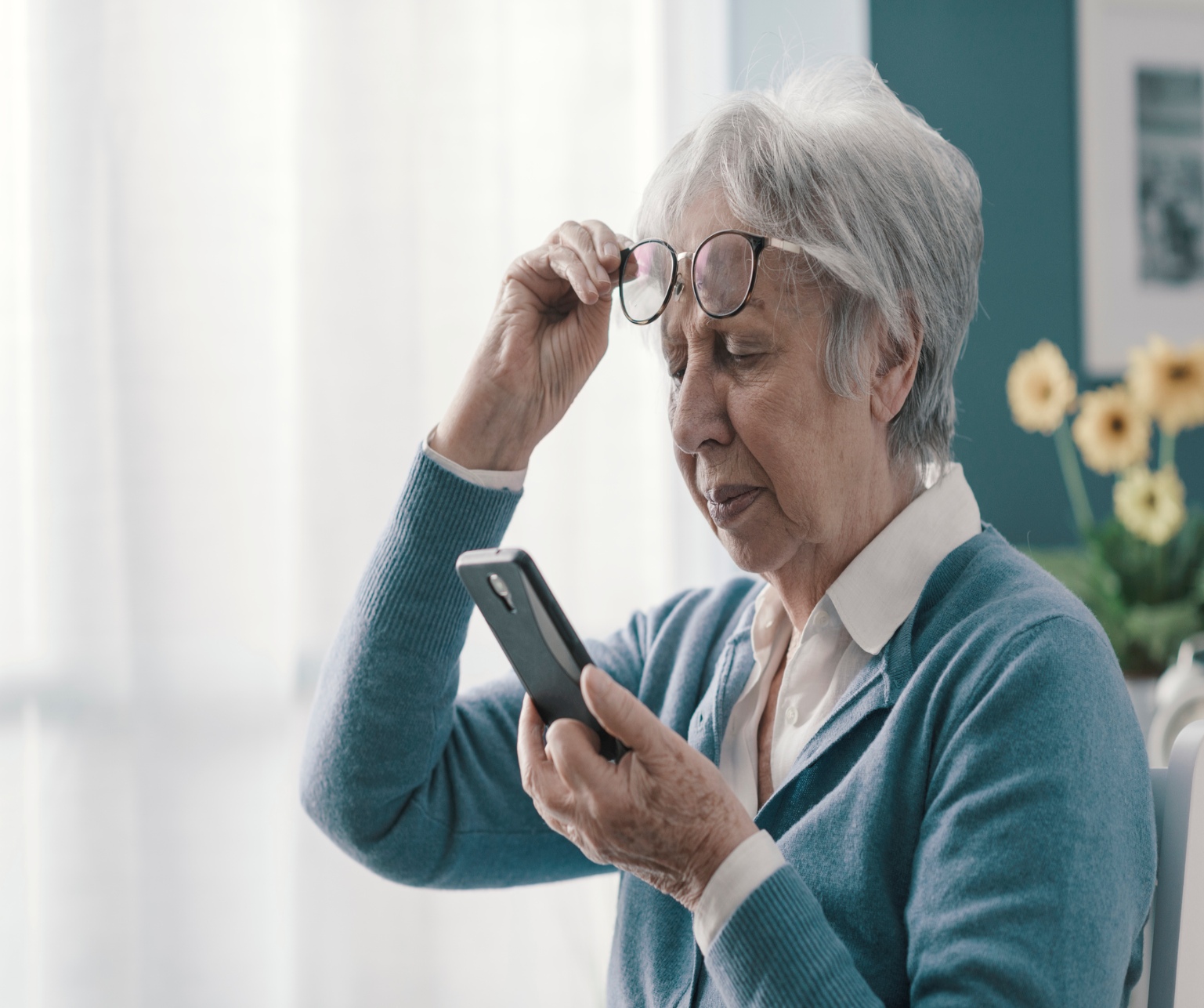 Elderly woman adjusting glasses to read smartphone, highlighting challenges with age-related vision problems.