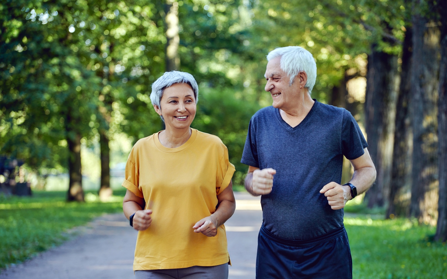 Elderly couple jogging in park to prevent eye problems like macular degeneration, showcasing active lifestyle for eye health after 50.