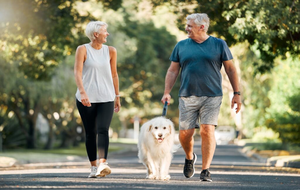 An elderly couple walking outdoor with their dog