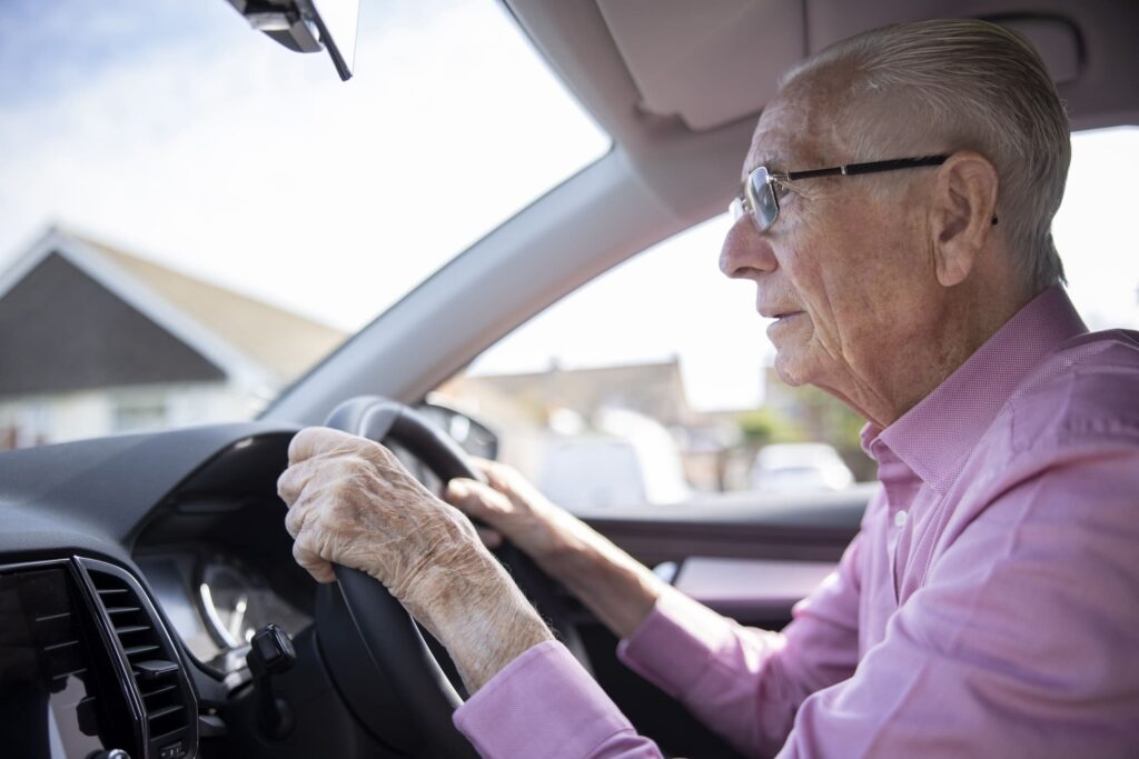 Elderly man with glasses driving a car, concentrating on the road ahead.