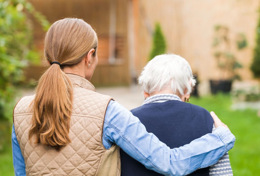 Woman with her arm around an elderly woman, walking together outdoors.