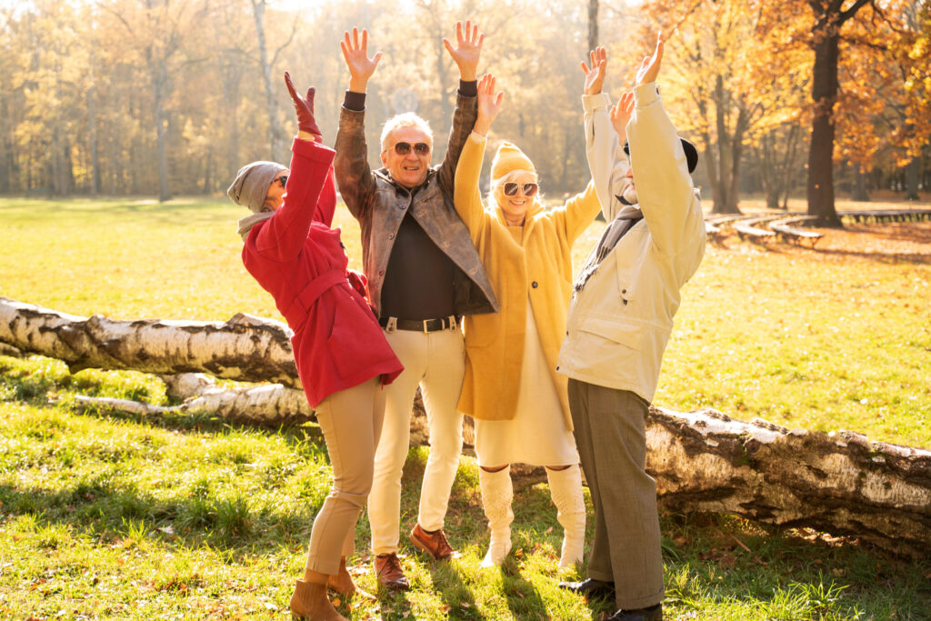 Group of seniors enjoying a sunny day outdoors, raising their arms in joy and wearing sunglasses.