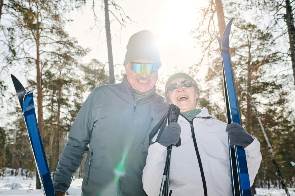 Senior couple wearing sunglasses and ski gear, smiling while enjoying a sunny day on the slopes.