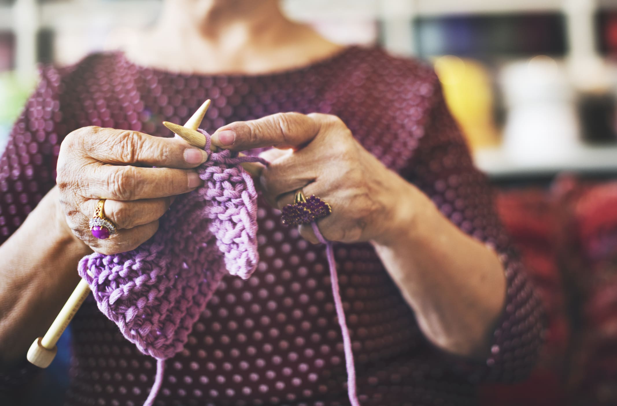 Close-up of a woman's hands knitting a purple scarf with wooden knitting needles, showcasing intricate details and focus.