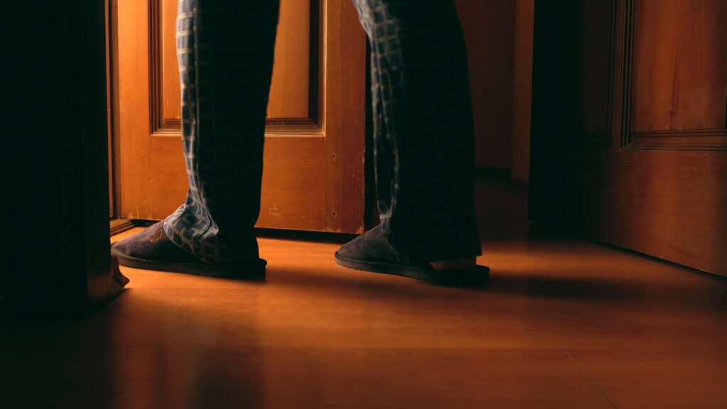 Close-up of a person in pajamas and slippers walking in dim indoor lighting, representing challenges of navigating spaces with night blindness.