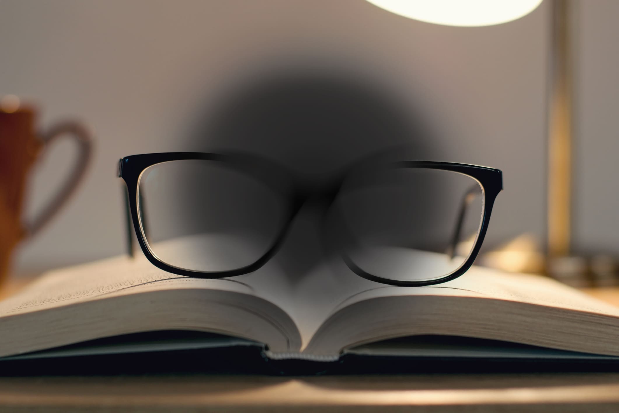 A pair of black-framed glasses resting on an open book, with the central area blurred to simulate vision loss.