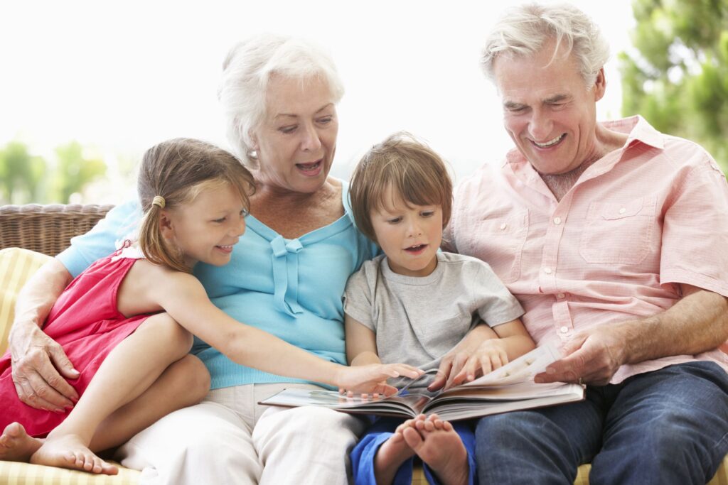 A happy family with grandparents and two young children reading a book together, symbolizing the importance of family history in genetics and age-related macular degeneration (AMD).