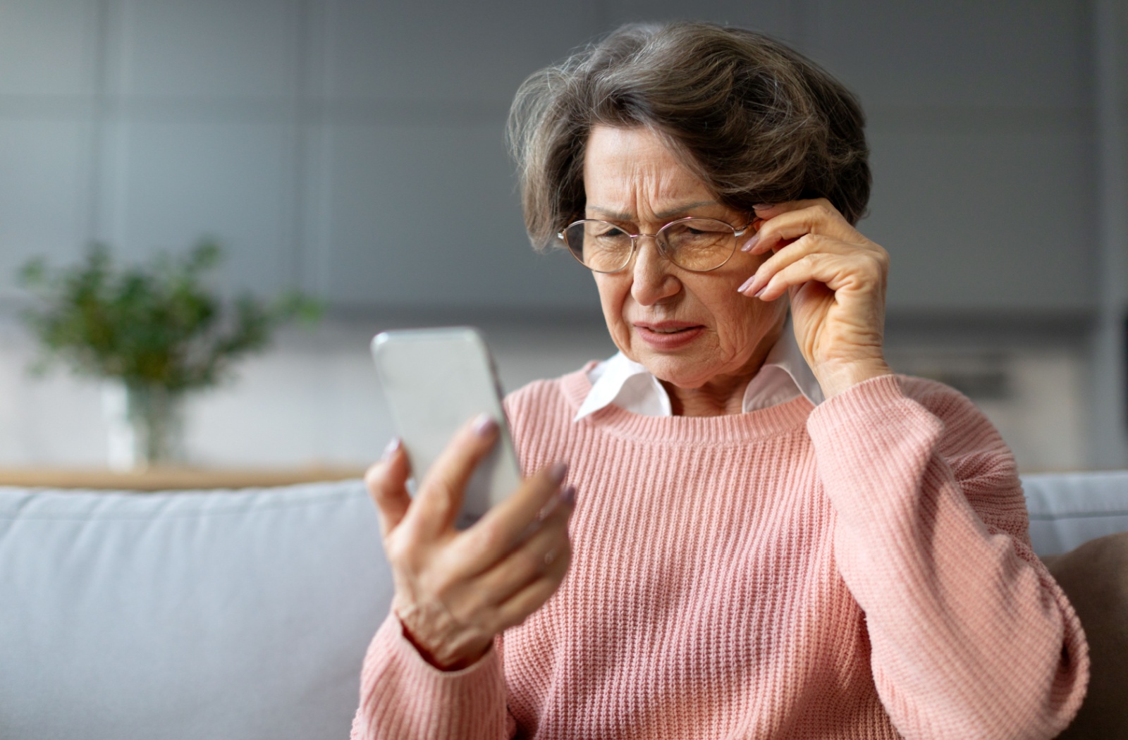 An elderly person wearing glasses and squinting at their phone screen.